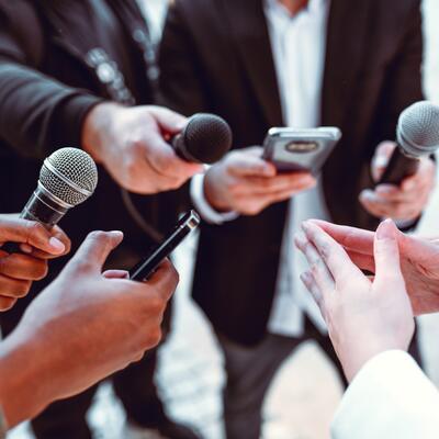 Reporters hold up microphones while listening to a person speak
